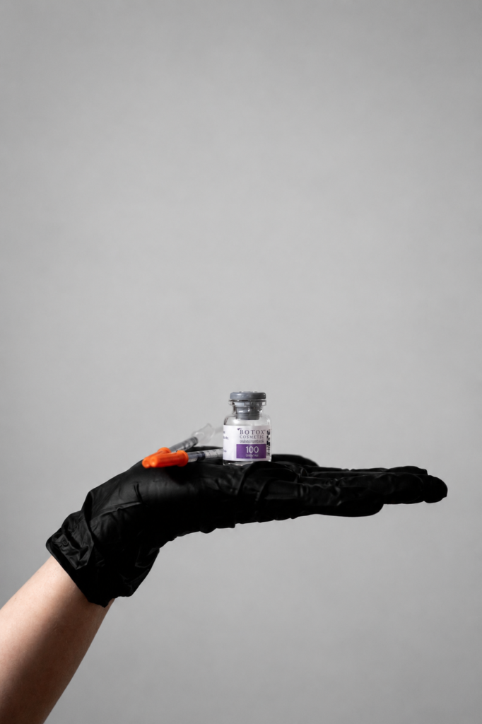 A BOTOX Cosmetic vial and syringes on a gloved hand.