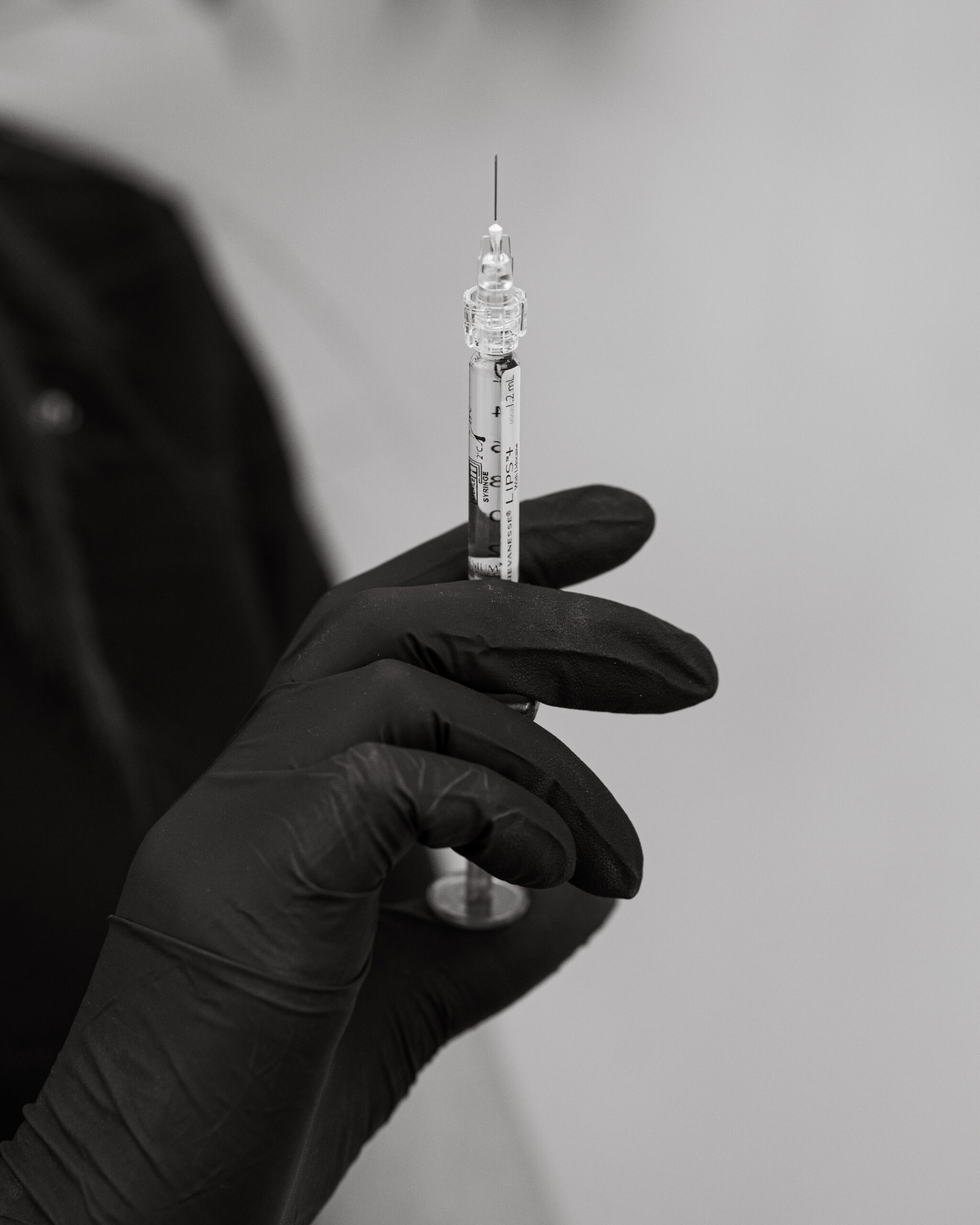 A gloved practitioner holding a Revanesse Lips+ syringe.