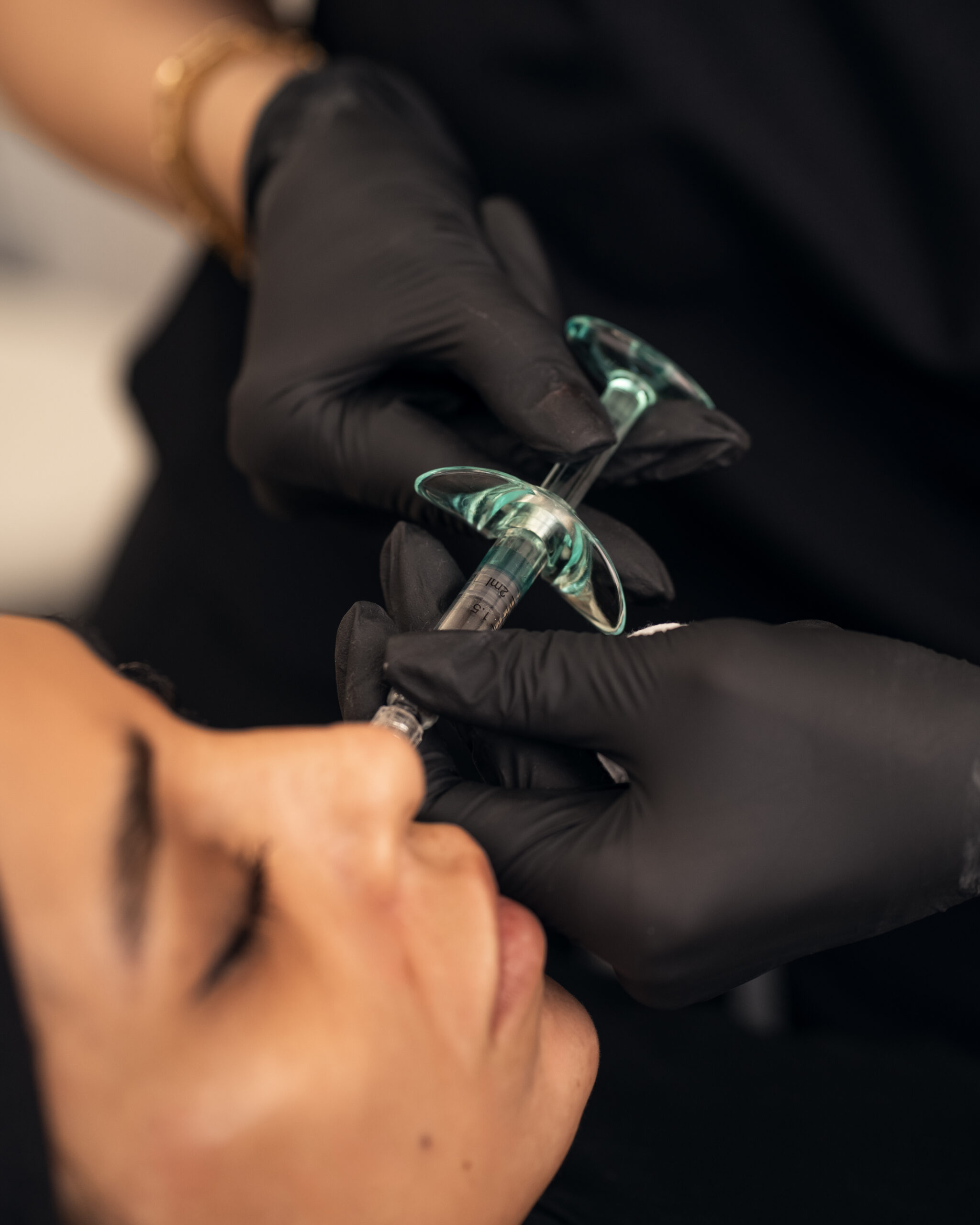 A gloved practitioner holding a syringe near a client’s lips.