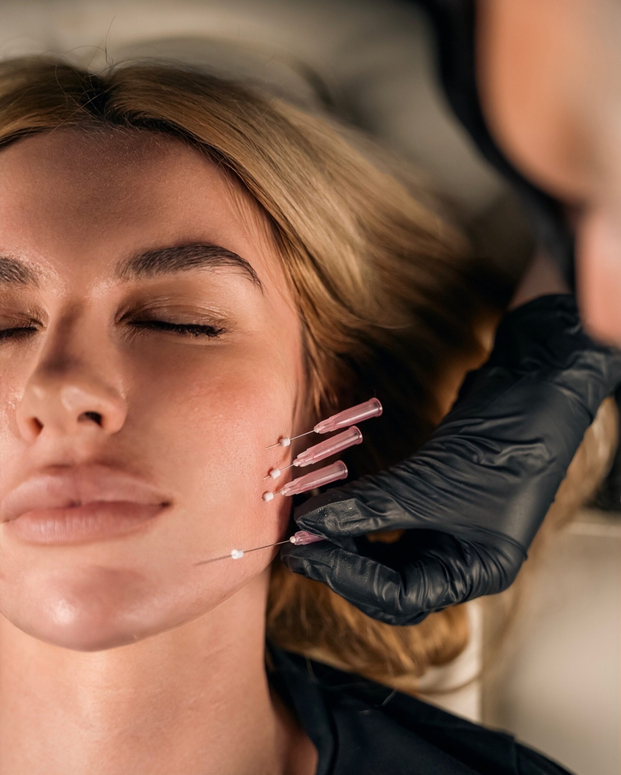 A gloved practitioner supporting a client’s cheek during a facial procedure.