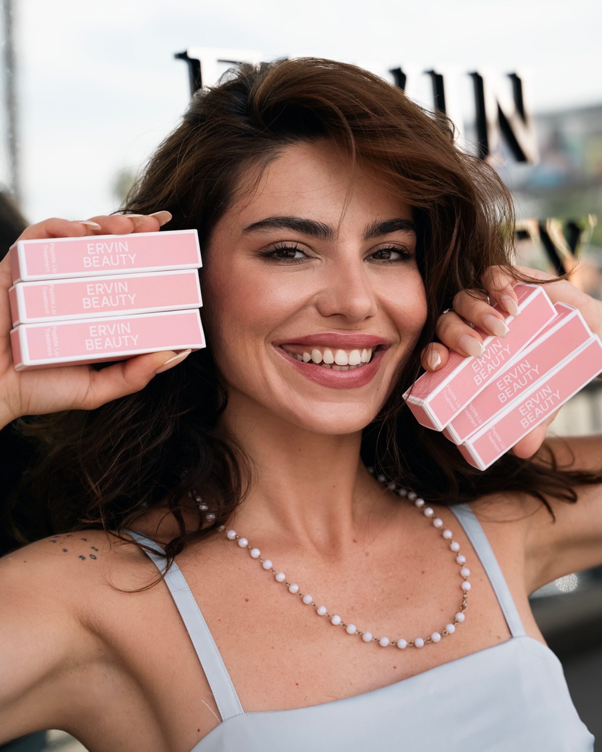 Smiling woman holding Ervin Beauty lip-care products in the clinic.
