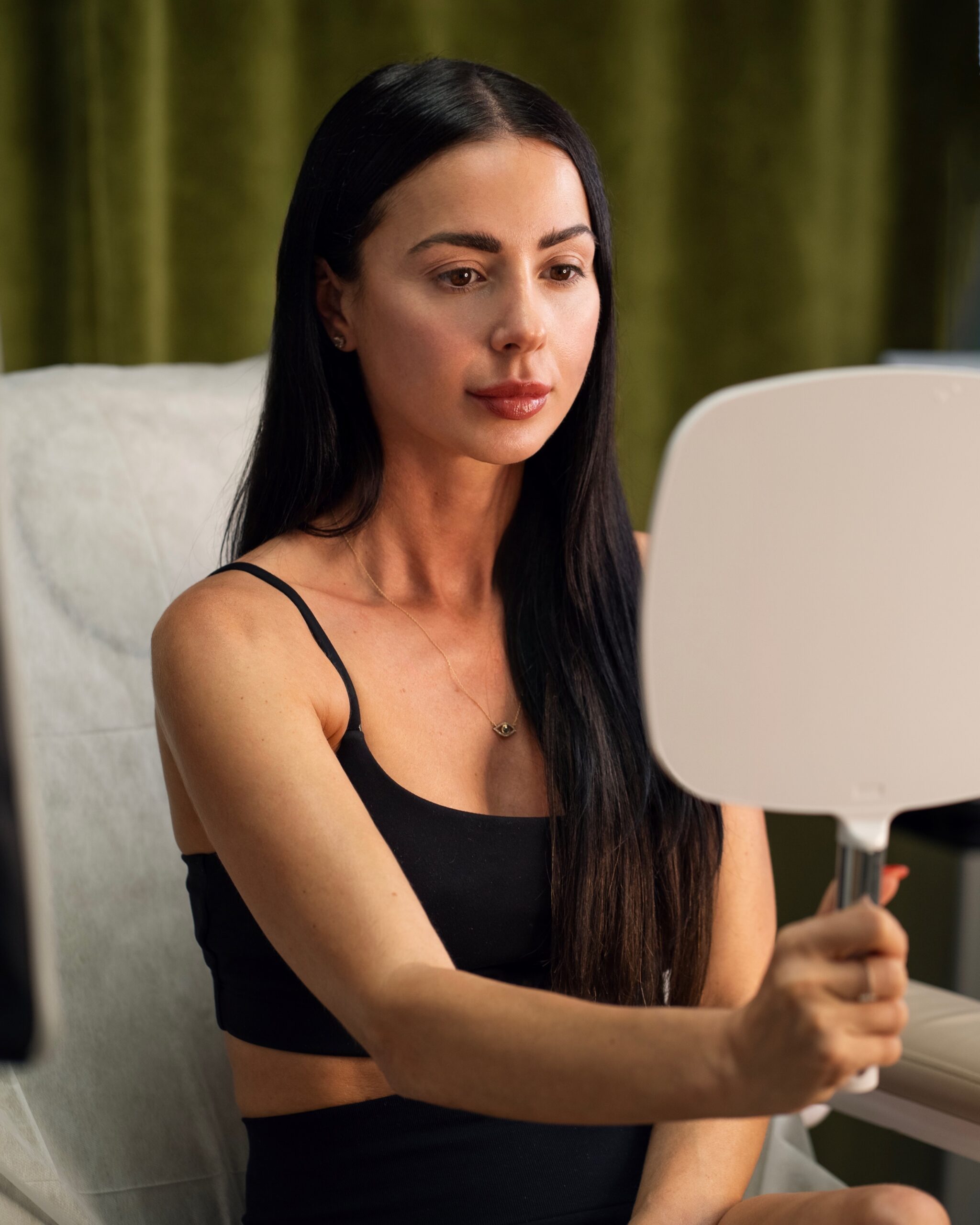 Woman seated with a handheld mirror at Ervin Beauty