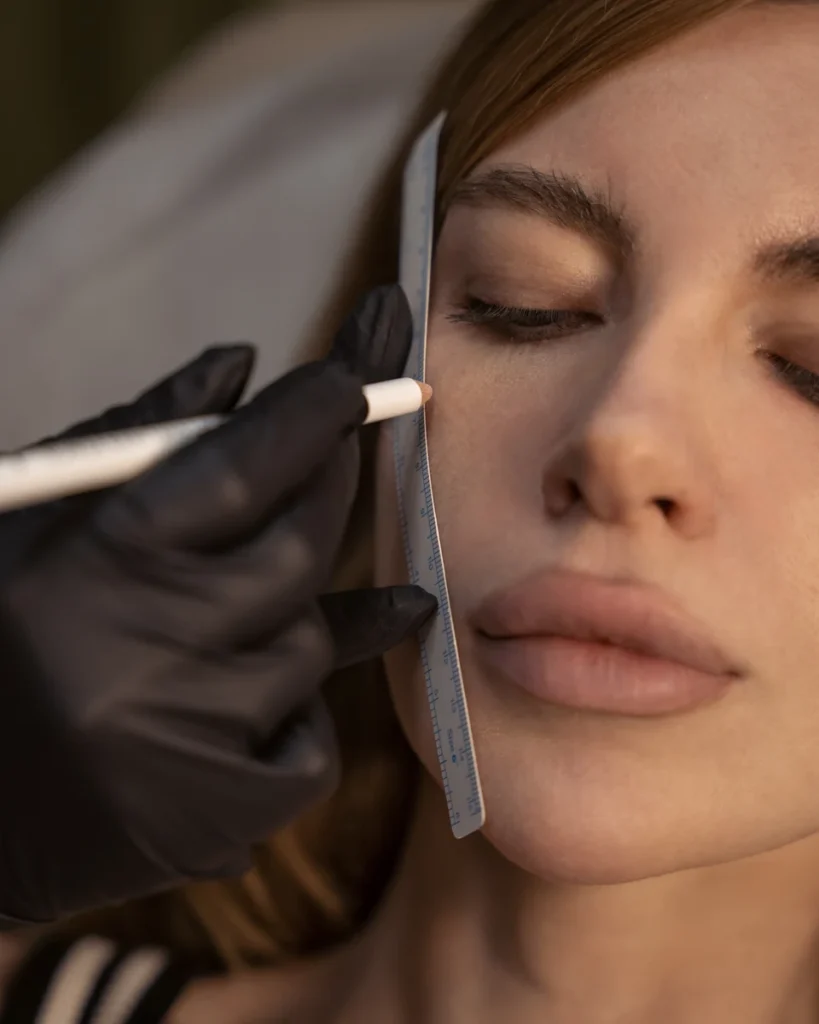 Gloved hands measuring and marking a woman’s cheek.